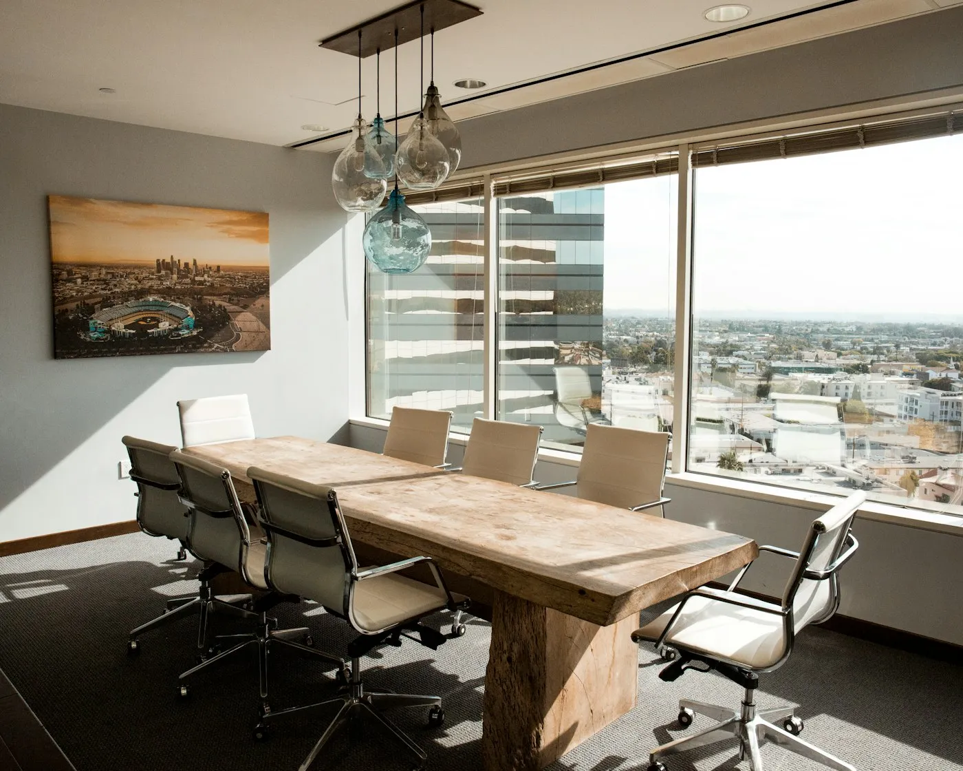 Sunlit commercial boardroom with a substantial wood table, leather chairs, and city views